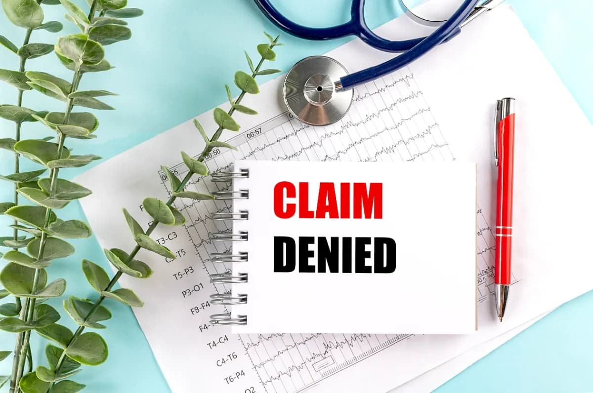Claim denied stamp on medical notepad with stethoscope and health insurance chart
