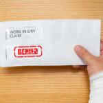 wrapped hand holding an envelope with a work injury claim application inside stamped with denied