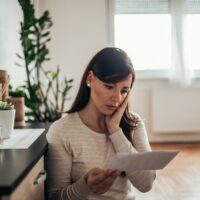 Stressed woman reading a letter at home.