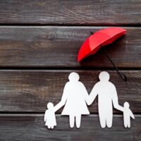 Live insurance concept. Family silhouette protected by umbrella on dark wooden background top-down copy space Live insurance concept. Family silhouette protected by umbrella on dark wooden background top-down copy space