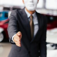 Dishonest and evil salesman in business suit in car dealership company handshaking welcome customers to exploit and deceive customers - fraud and bad quality service in business concept