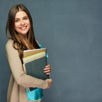 Smiling woman teacher portrait on gray wall.