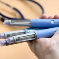 Women's hands holding lots of blue Insulin injection pen for diabetics and weight loss.