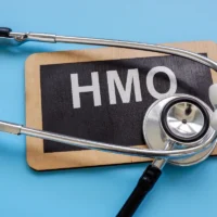 Stethoscope on a small blackboard with "HMO" written in white, set against a light blue background. The image conveys healthcare and organization. Stethoscope on a small blackboard with "HMO" written in white, set against a light blue background. The image conveys healthcare and organization.