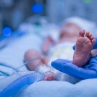 Blue gloved nurse hand holding premature newborn baby foot in intensive care unit